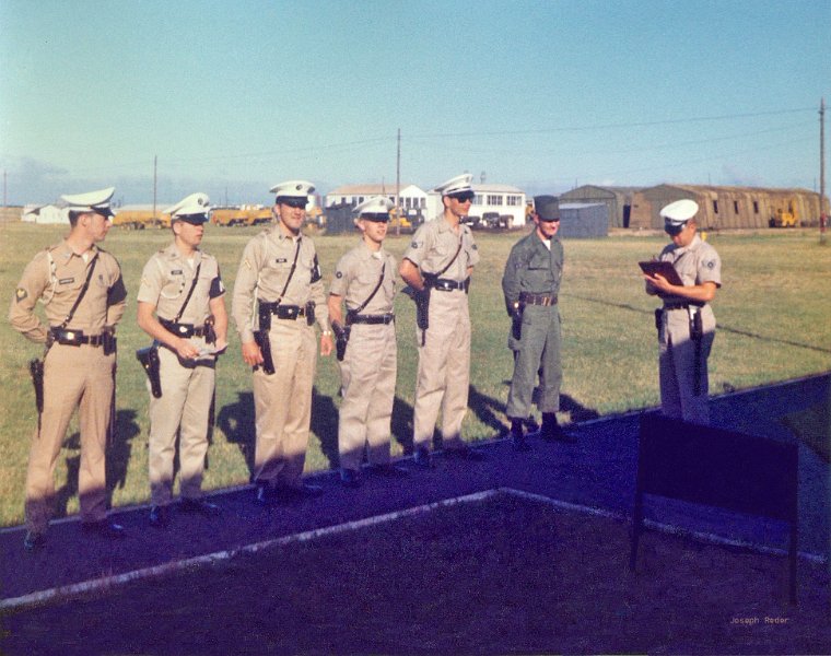 A_flight.jpg - This was probably taken in 1962.  We were not an Air Police Squadron but a section of the 7305th.  Left to right are:  SP4 Ned Hartsough, PFC David Green, PFC Jerry Calisi, A3C Joseph Reder, A1C Jack Card, A2C Verlon Miller and SSGT Harol Von Draughn (sp?) flight sgt.  Taken behind the APO.